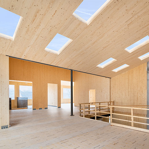 Hell erleuchteter Raum des Kinderhortes in Mering mit moderner Holzarchitektur, Oberlichtern und einem Treppengeländer im Vordergrund.