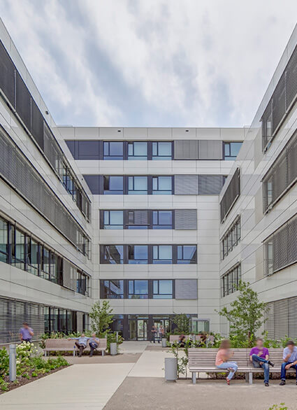 Außenansicht Audi Ingolstadt - Innenhof eines modernen Bürogebäudes mit grauer Fassade und grossen Fenstern und bepflanzten Beeten